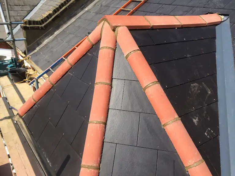 A roof that has some orange ridge tiles on it.